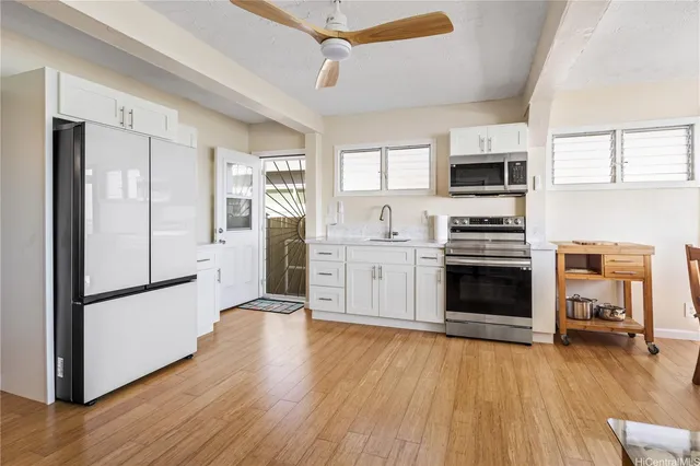 a kitchen with stainless steel appliances a stove top oven a sink a refrigerator white cabinets and wooden floor