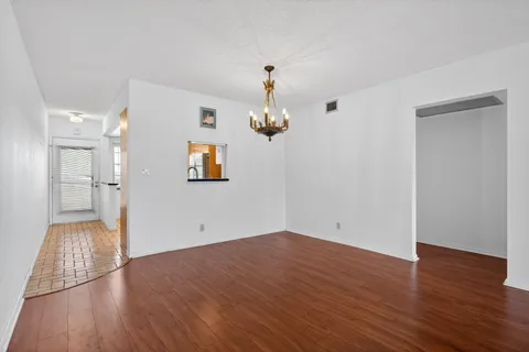 a view of empty room with wooden floor and kitchen view