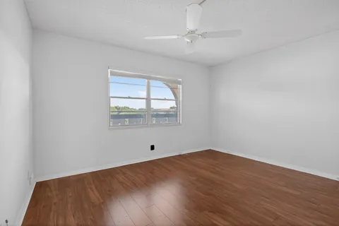 an empty room with wooden floor chandelier fan and windows