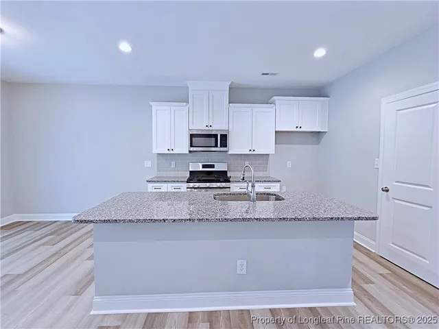 a kitchen with granite countertop a sink a stove a microwave a counter top space and cabinets