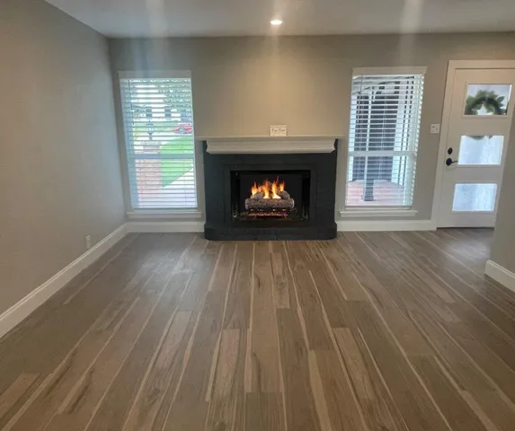 a view of an empty room with wooden floor fireplace and a window