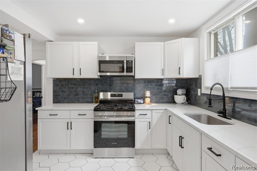 4612 Balfour Road Detroit, MI 48224 - Photo 6 of 20 Modern kitchen featuring white shaker-style cabinetry with black hardware, stainless steel appliances, a dark subway tile backsplash, and white hexagonal floor tiling