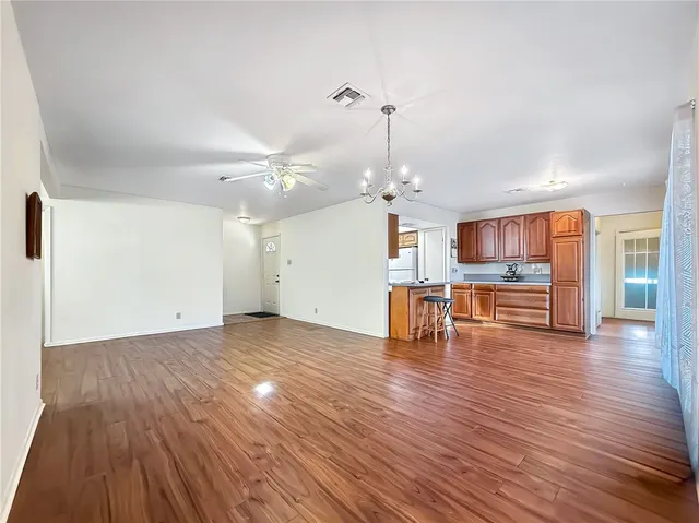 a view of an empty room with wooden floor and kitchen view