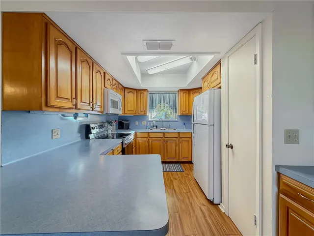 a kitchen with stainless steel appliances granite countertop a refrigerator a sink dishwasher a stove and white countertops with wooden floor