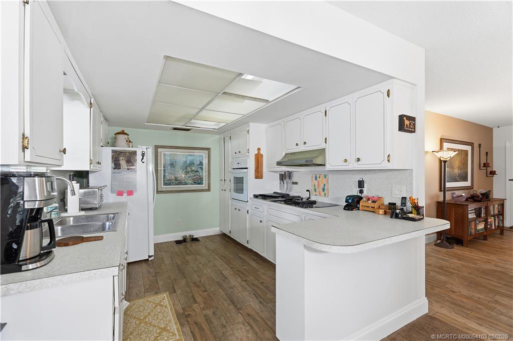 900 Northwest 11th Terrace Stuart, FL 34994 - Photo 22 of 35 a kitchen with stainless steel appliances a stove top oven a sink a refrigerator white cabinets and wooden floor