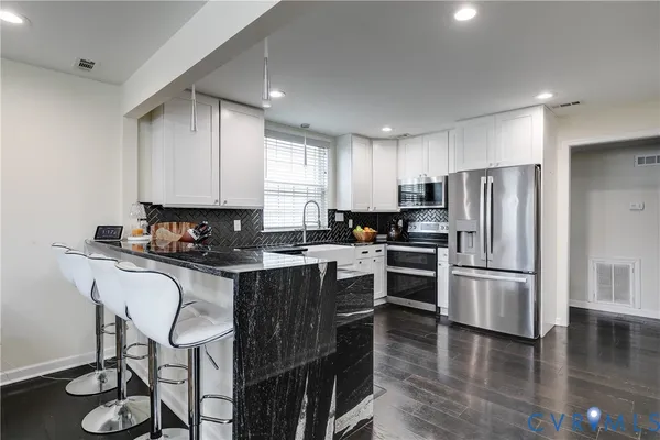 a kitchen with kitchen island granite countertop stainless steel appliances a sink a stove a refrigerator cabinets and dining table