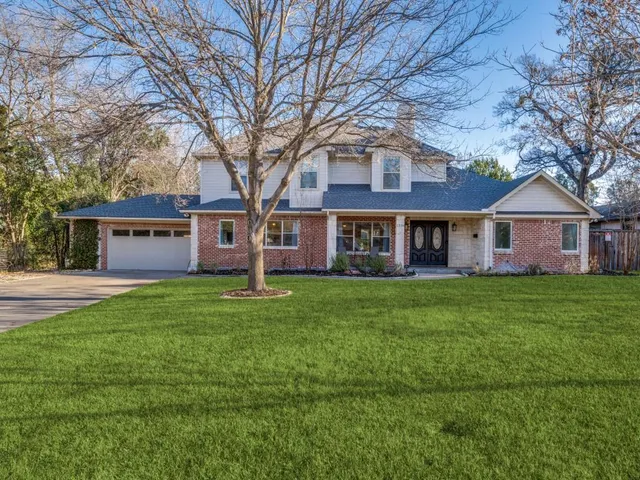 a view of a brick house with a big yard large trees and a large tree