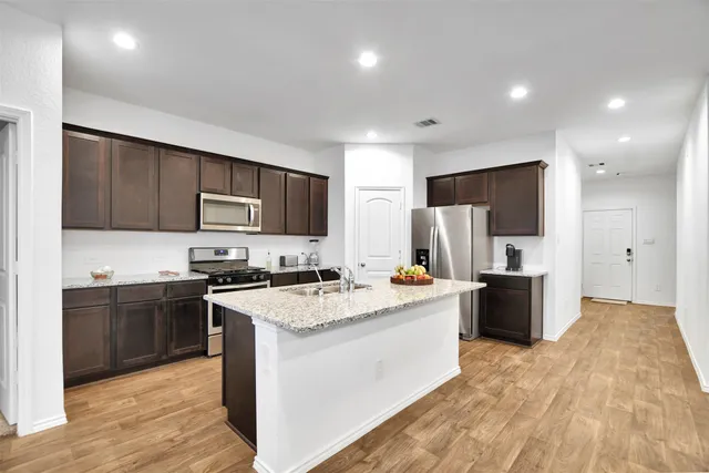 a kitchen with stainless steel appliances granite countertop a sink dishwasher and a refrigerator with wooden floor