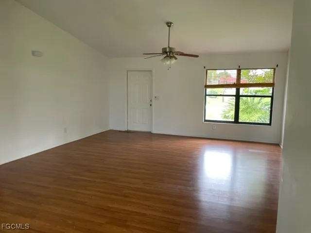 an empty room with wooden floor chandelier fan and windows
