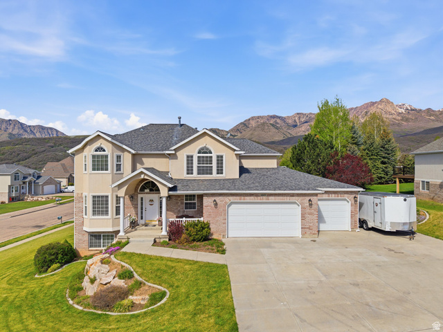 Two-story residence featuring a tan stucco and brick facade with a prominent arched entry, multiple arched windows, and a three-car garage