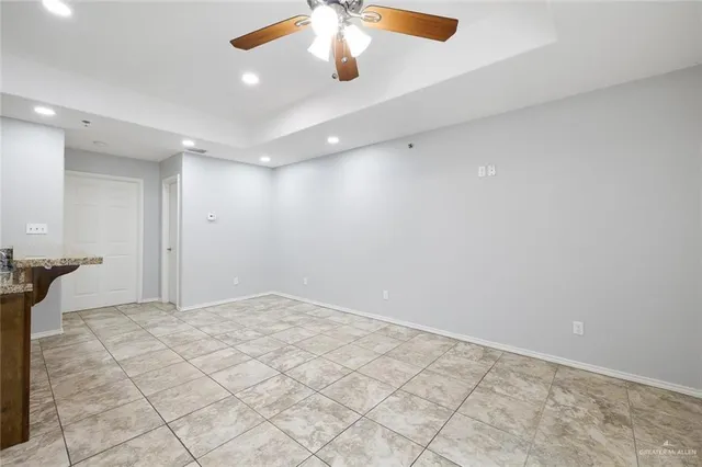 an empty room with chandelier fan and kitchen view