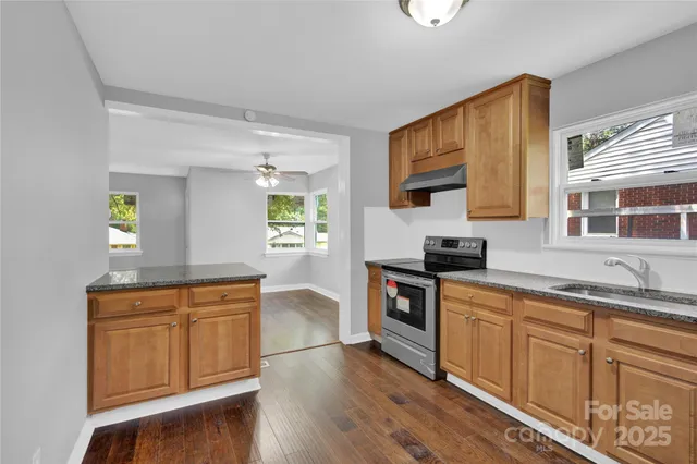 a kitchen with stainless steel appliances granite countertop a sink a stove a microwave a sink and white cabinets with wooden floor