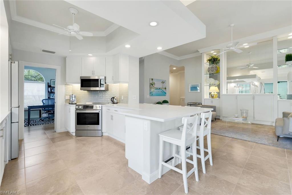 7063 Toscana Court Naples, FL 34114 - Photo 17 of 47 Kitchen featuring ceiling fan, a peninsula, ornamental molding, appliances with stainless steel finishes, and white cabinets