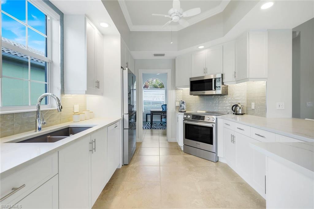 7063 Toscana Court Naples, FL 34114 - Photo 18 of 47 Kitchen featuring stainless steel appliances, white cabinets, backsplash, light stone counters, and a ceiling fan