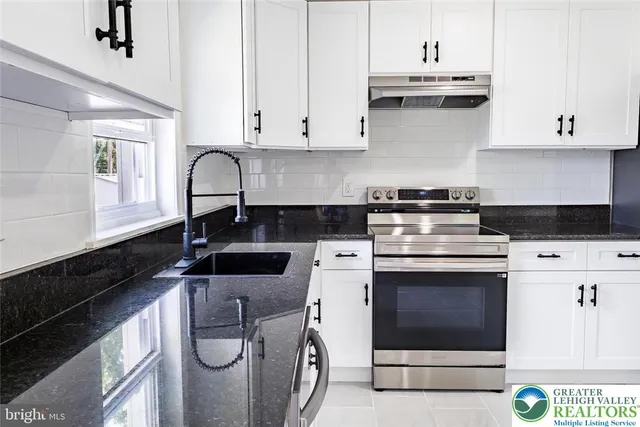a kitchen with stainless steel appliances granite countertop a stove a sink and white cabinets