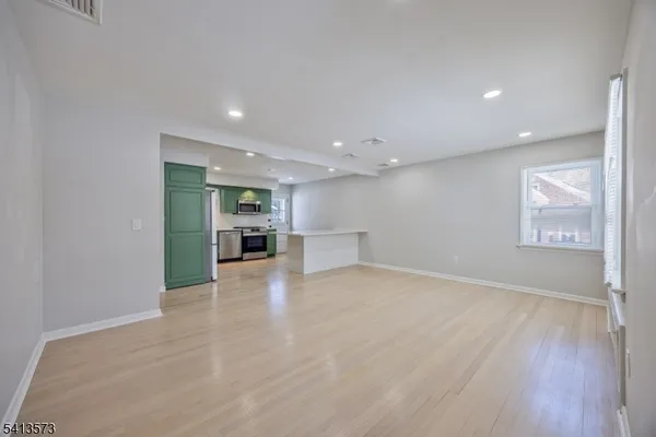 a view of an empty room with wooden floor kitchen view and a window