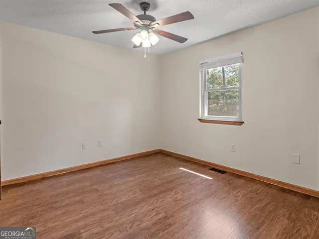 an empty room with wooden floor chandelier fan and windows