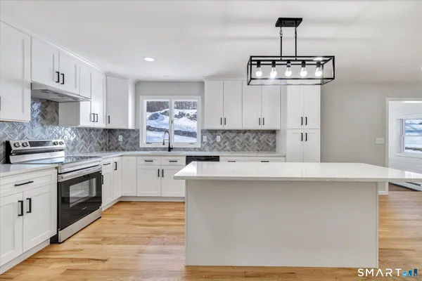 a kitchen with stainless steel appliances a stove a sink dishwasher a refrigerator and white cabinets with wooden floor