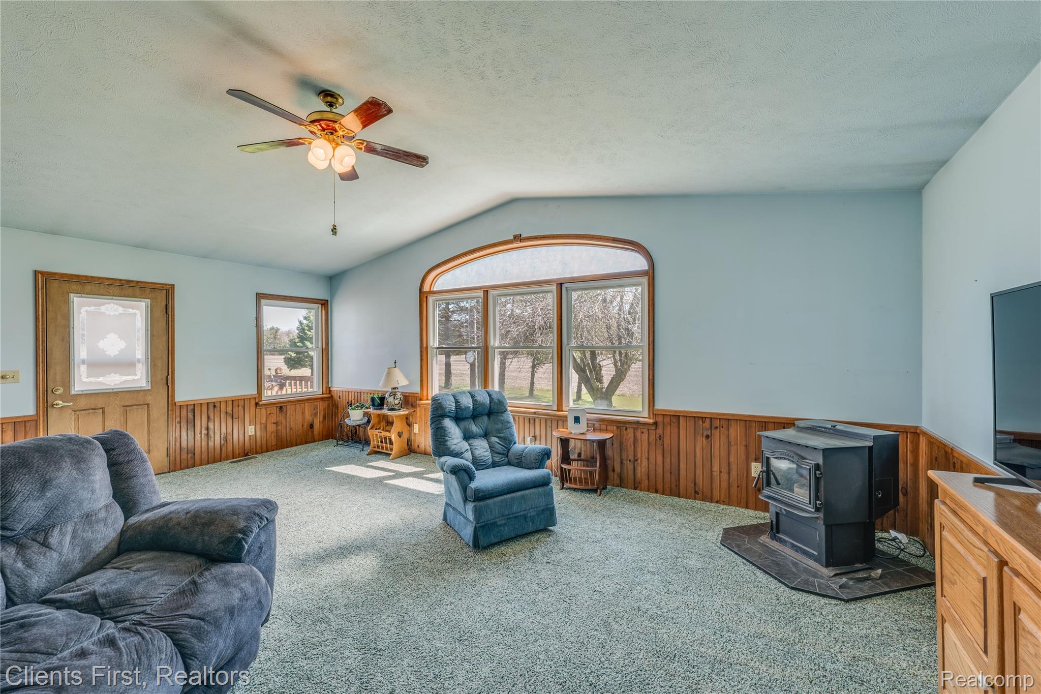 342 North Chambers Road Tawas City, MI 48763 - Photo 7 of 30 Carpeted living area featuring wood walls, wainscoting, ceiling fan, and a wood stove