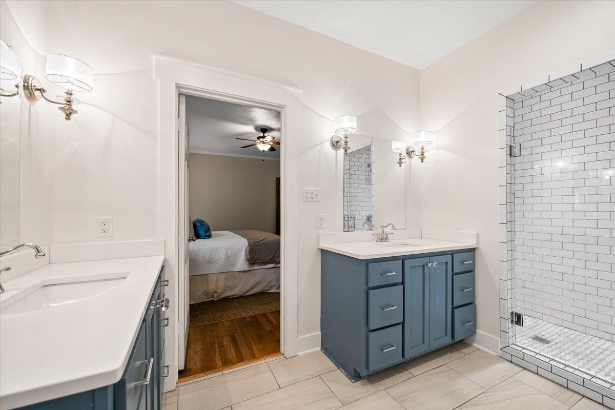1273 Brookfield Road Memphis, TN 38119 - Photo 24 of 40 Bathroom featuring dual vanities with blue cabinetry and white countertops, a walk-in shower with subway tile surround, tile flooring, and wall-mounted sconces