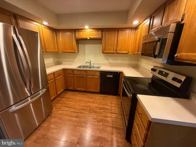 a kitchen with stainless steel appliances granite countertop a refrigerator a sink dishwasher a stove and white countertops with wooden floor