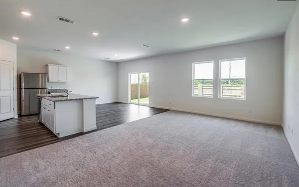 an empty room with windows and kitchen view