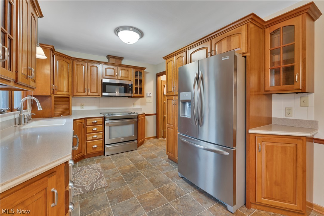 6599 Struthers Road Youngstown, OH 44514 - Photo 12 of 29 Kitchen featuring glass fronted cabinets, stainless steel appliances, wood finish cabinets, tasteful backsplash, and stone finish floors