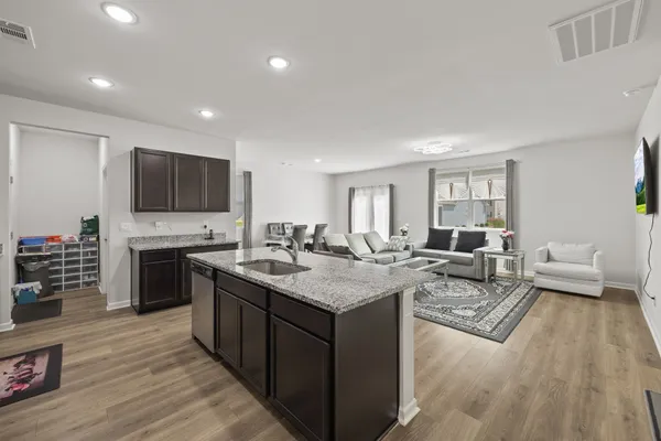 a open kitchen with stainless steel appliances granite countertop a stove top oven a sink dishwasher a dining table and chairs with wooden floor