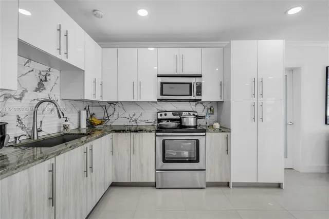 a kitchen with stainless steel appliances granite countertop white cabinets a sink a stove a refrigerator and a microwave