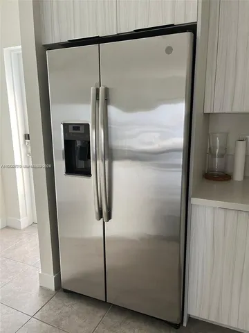 a close view of a refrigerator in kitchen and an empty room with wooden floor