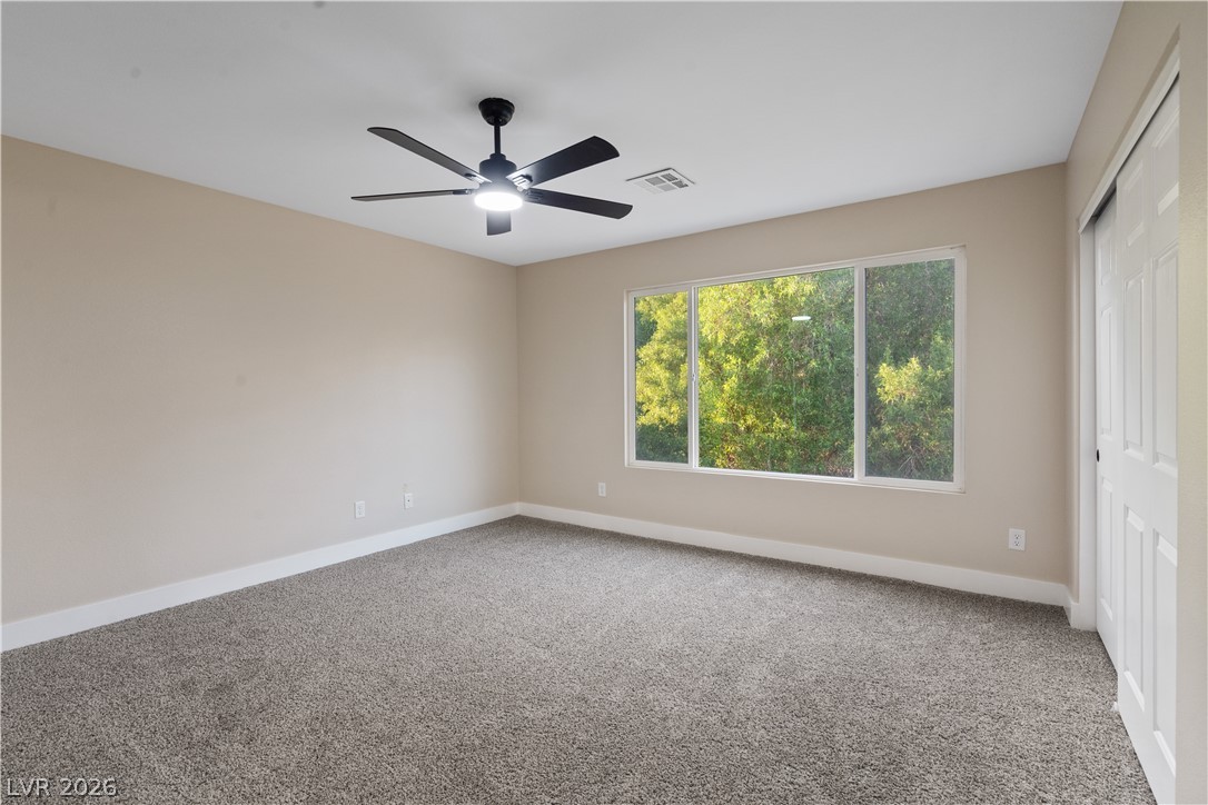 1662 Ravanusa Drive Henderson, NV 89052 - Photo 26 of 74 A spacious bedroom with a ceiling fan and large windows framing lush green foliage.