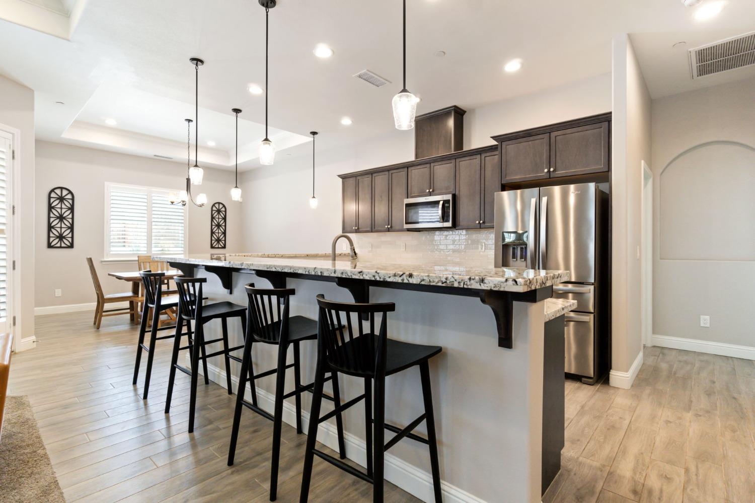 639 Mesa Drive Madera, CA 93636 - Photo 11 of 33 a kitchen with stainless steel appliances granite countertop a kitchen island a stove a refrigerator a sink a dining table and chairs with wooden floor