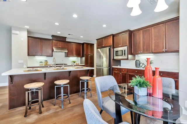 a kitchen with stainless steel appliances granite countertop a refrigerator a stove a sink a dining table and chairs with wooden floor