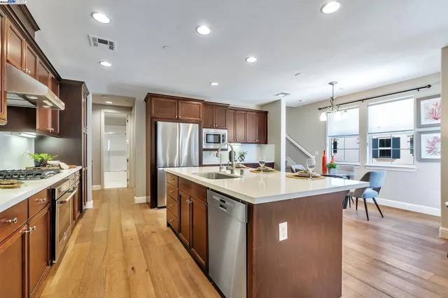 a kitchen with stainless steel appliances a stove a sink a refrigerator and a dining table with wooden floor