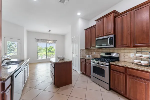 a kitchen with granite countertop kitchen island stainless steel appliances a sink a stove top oven a counter space and cabinets