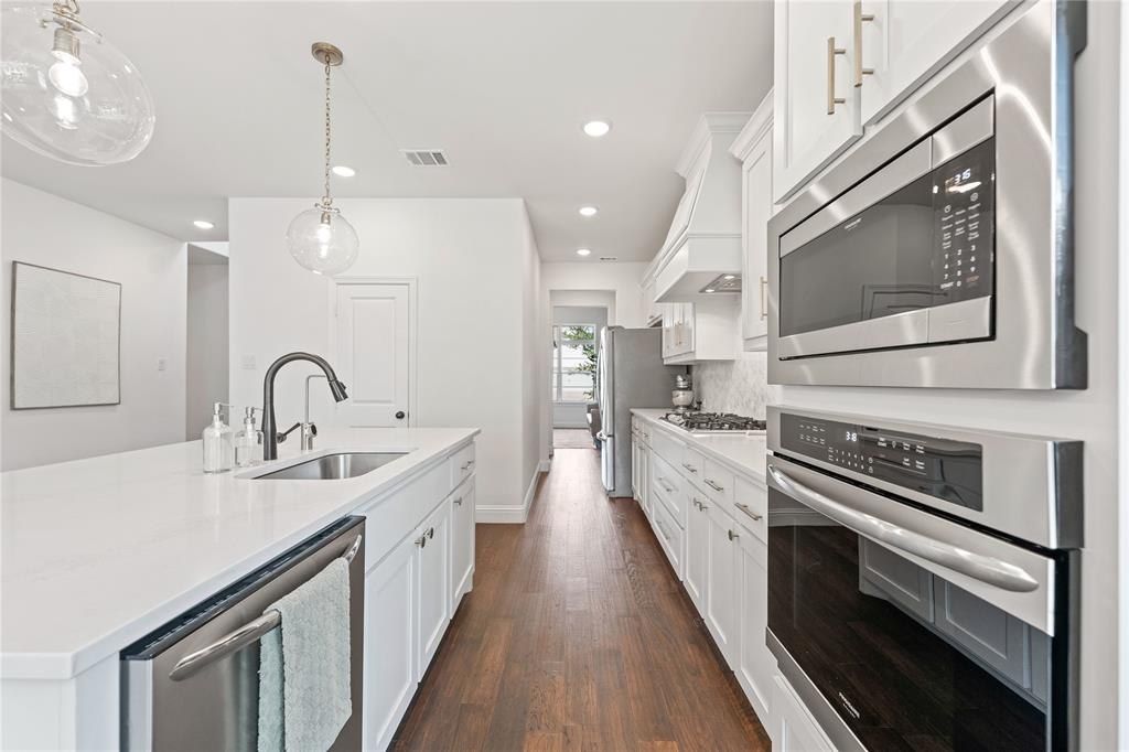 5244 Ranchero Trail Fort Worth, TX 76126 - Photo 8 of 33 Kitchen featuring white cabinets, appliances with stainless steel finishes, an island with sink, hanging light fixtures, and dark wood-type flooring