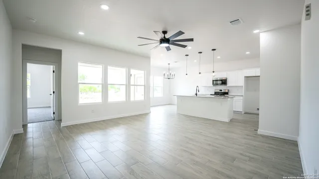 a view of an empty room and kitchen with wooden floor