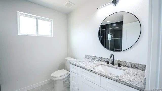 a bathroom with a granite countertop toilet sink and mirror
