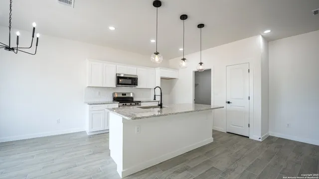 a kitchen with stainless steel appliances granite countertop a sink a stove a refrigerator and white cabinets with wooden floor