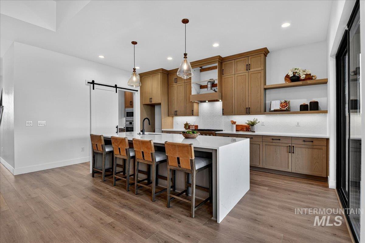 7714 West Flathead Lake Street, Unit ASPEN Eagle, ID 83616 - Photo 10 of 30 Kitchen with a barn door, brown cabinetry, a breakfast bar, a center island with sink, and open shelves