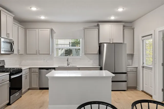 a kitchen with stainless steel appliances a sink a stove a refrigerator cabinets and a window