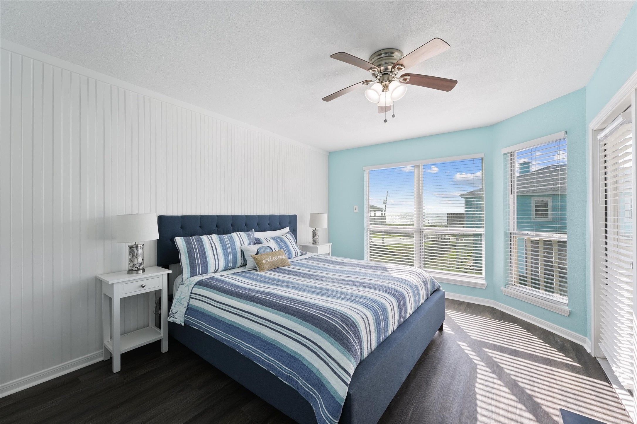17607 Termini-San Luis Pass Road Galveston, TX 77554 - Photo 20 of 42 The primary bedroom features soft blue walls and large windows, creating a bright and airy atmosphere. The spacious layout provides ample room for comfort, complemented by a cozy ceiling fan.
