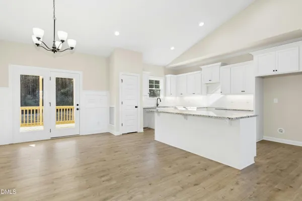 a large white kitchen with kitchen island a chandelier wooden floor and a refrigerator