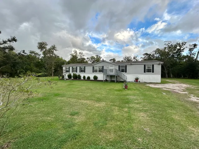 a view of a white house with a big yard and potted plants
