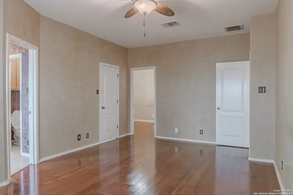 an empty room with wooden floor chandelier fan and windows