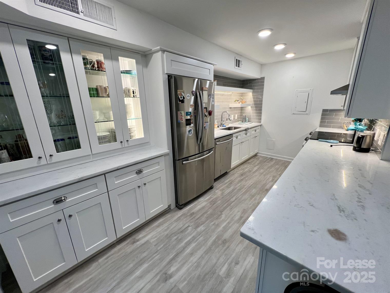 a kitchen with granite countertop a refrigerator a sink and white cabinets
