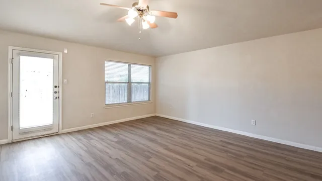 a view of an empty room with wooden floor and a window