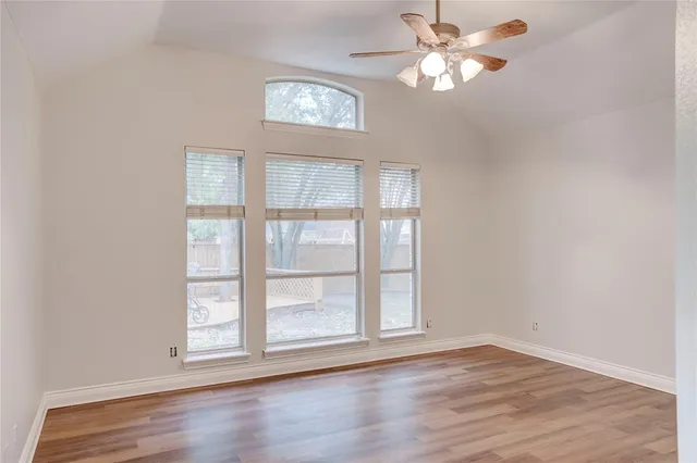 an empty room with wooden floor chandelier fan and windows