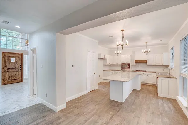 a large white kitchen with a refrigerator a stove a sink dishwasher and a dining table with wooden floor