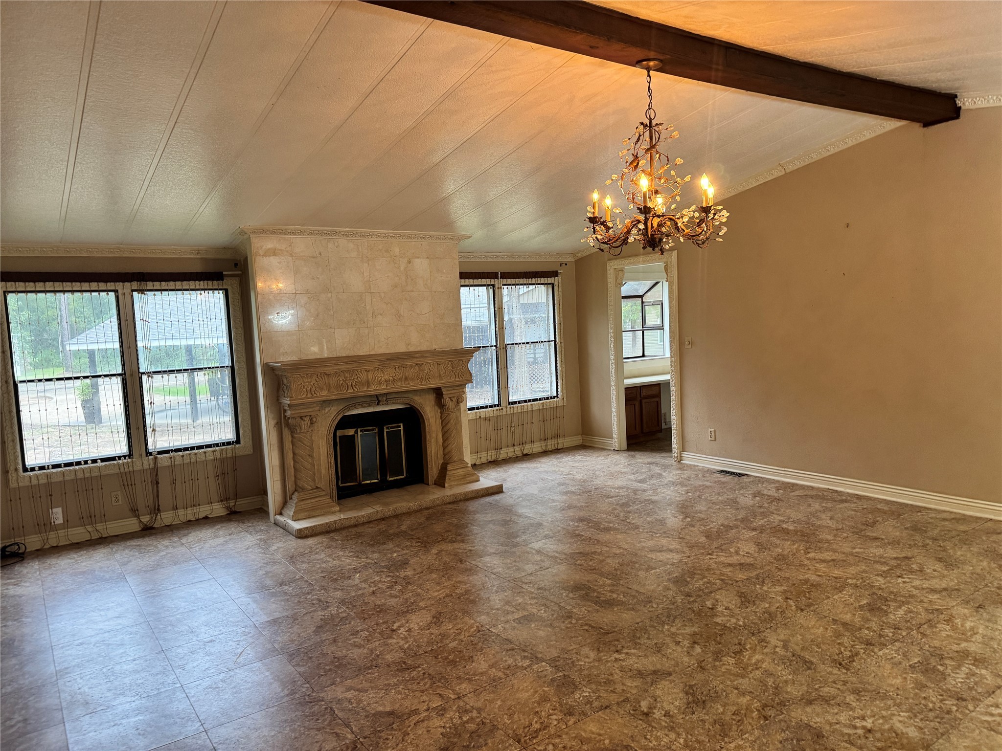 106 Westlake Road Trinity, TX 75862 - Photo 11 of 36 Spacious living area with a high ceiling and exposed beam. Features a large, elegant fireplace and a classic chandelier. Natural light flows in through multiple windows, enhancing the room's warm tones and tiled flooring.